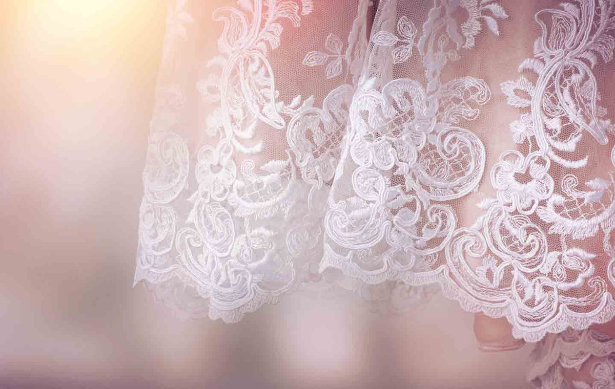 Close up of the scalloped hemline of a white lace wedding dress.